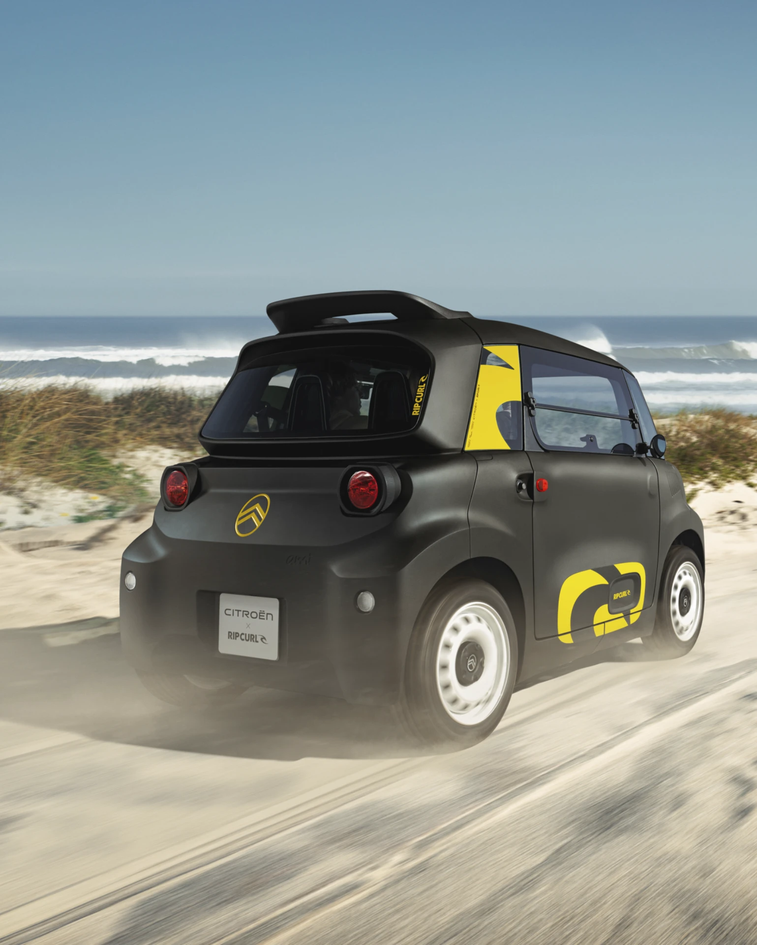 Vue trois‑quarts arrière en conduite de la Citroën Ami x Rip Curl électrique sans permis, Citroën Ami synonyme de conduite ludique pour une voiture électrique urbaine